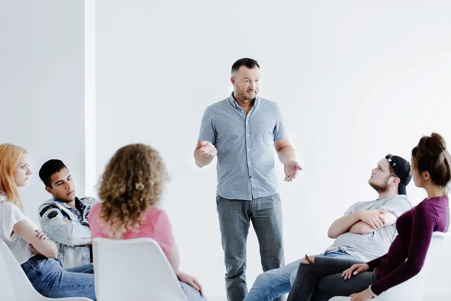 Therapist standing while leading a group therapy session with young adults seated in a circle during addiction treatment.
