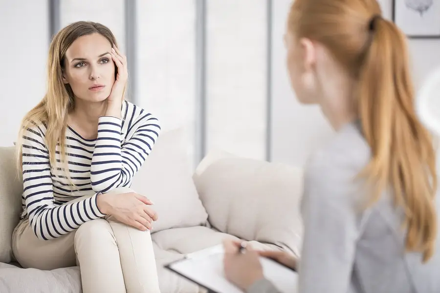 Woman in individual therapy session listening to a counselor taking notes on a couch in a calm office setting.