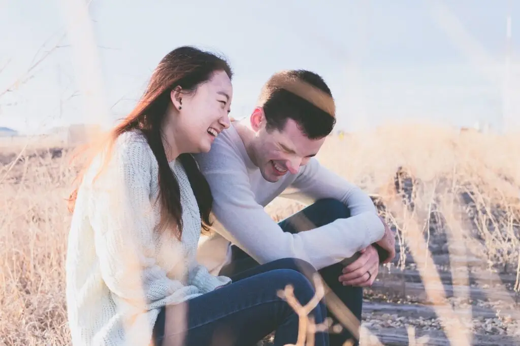 Couple laughing together outdoors in a sunny field, sharing a warm and hopeful moment in recovery.
